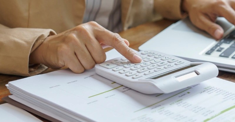 person's hands on a desk with a calculator, lap top, and papers
